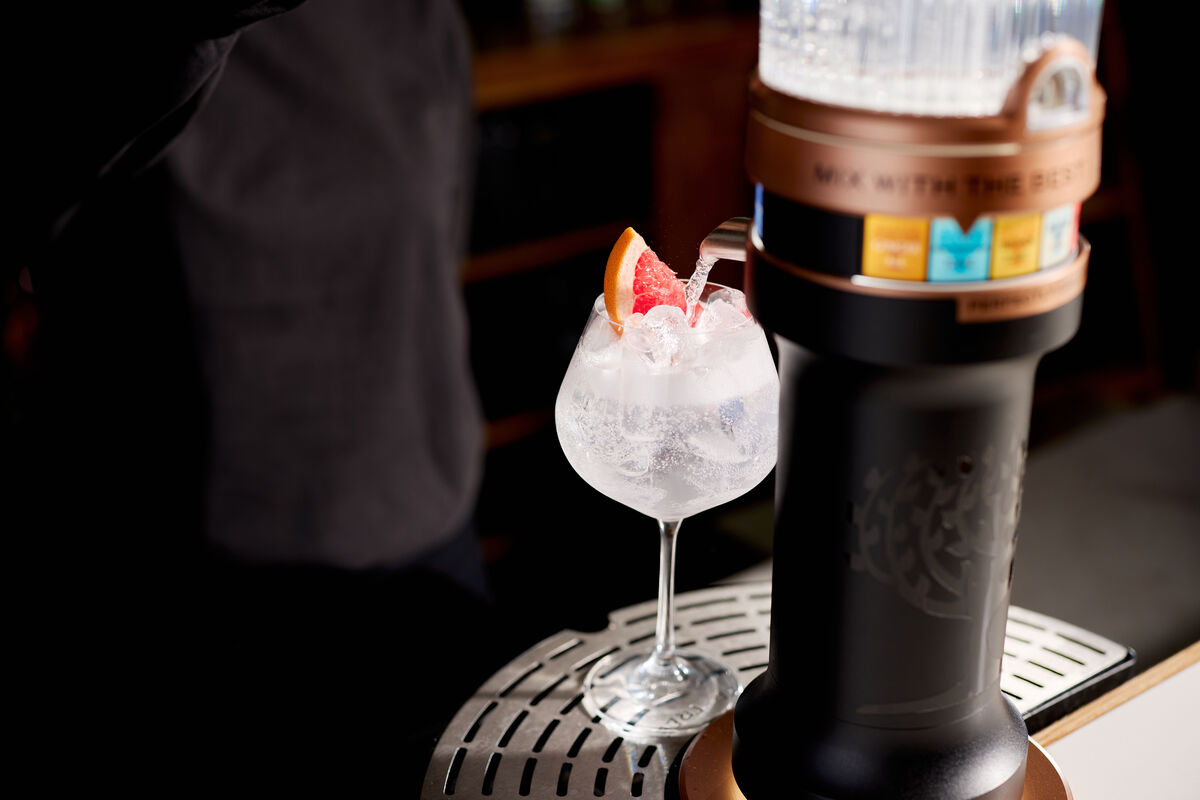 Close-up of the Fever-Tree tap pouring mixer into a garnished glass beside the dispenser